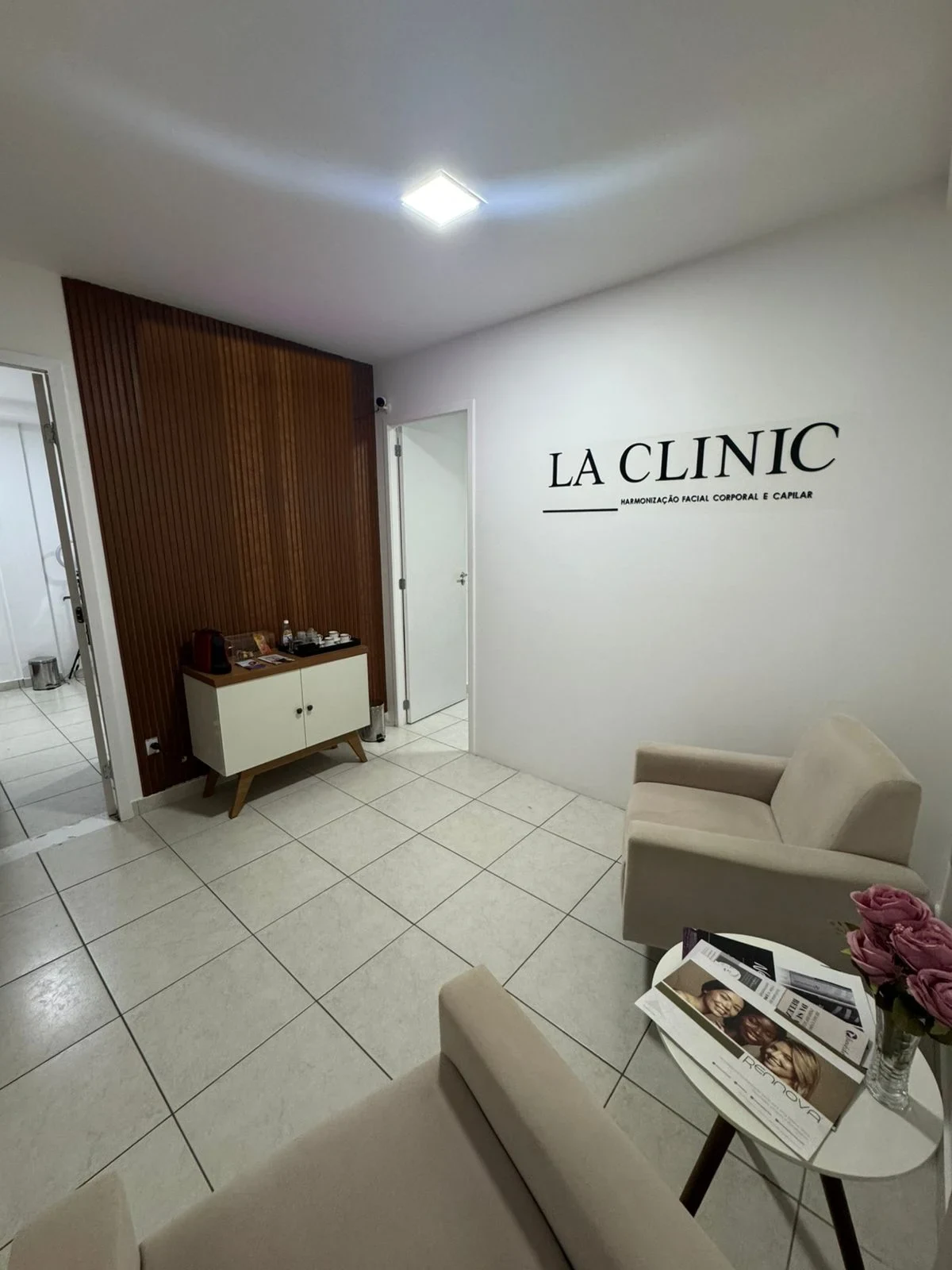 Recepção da LA CLINIC: aparador branco com cafeteira e xícaras diante de um painel ripado de madeira escura