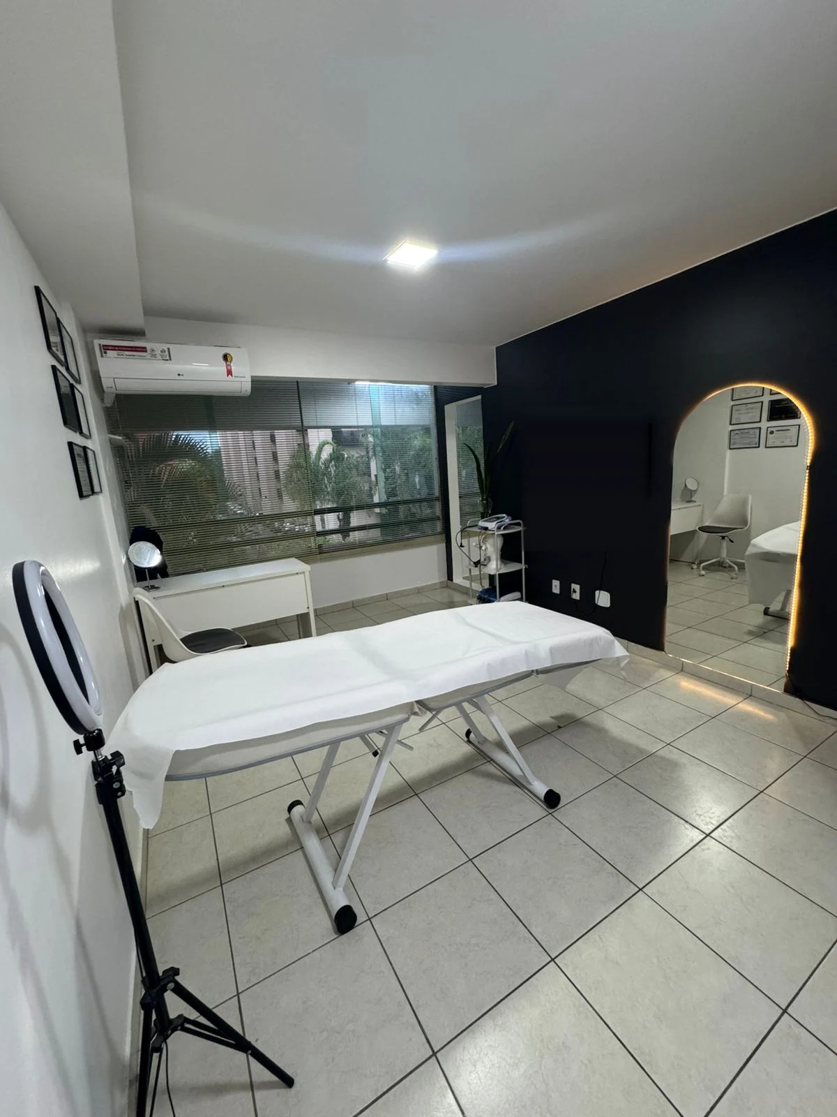 Sala de atendimento da LA CLINIC: maca branca ao centro, parede escura e espelho em arco contornado por um filete de luz